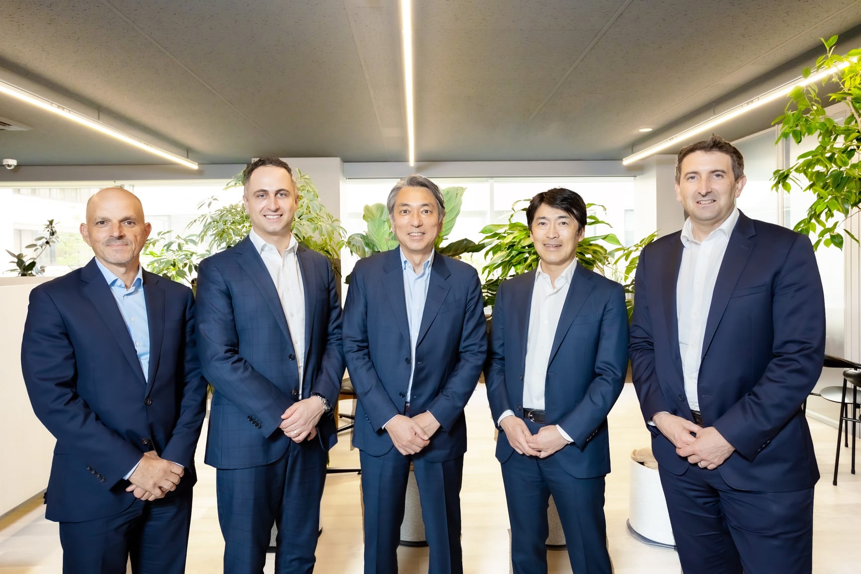 Photo of five men of differing nationalities all wearing navy blue suits and light blue or white business shirts.